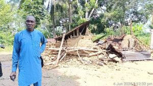 Village Head of Ukim Ita Eyo Ndem Community, Chief Samuel Ekpe-Ita, standing in front of the murder suspect's (Akaniyene Ignatius Eshiet), a destroyed property