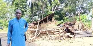 Village Head of Ukim Ita Eyo Ndem Community, Chief Samuel Ekpe-Ita, standing in front of the murder suspect's (Akaniyene Ignatius Eshiet), a destroyed property